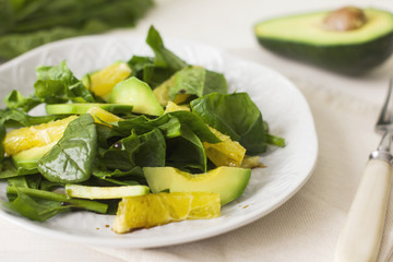 Raw salad of spinach, avocado and orange on a white wooden background
