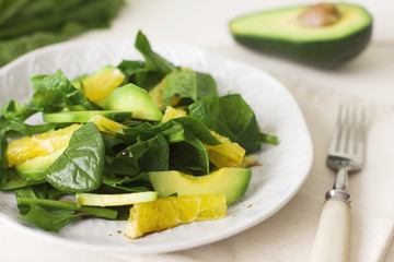 Raw salad of spinach, avocado and orange on a white wooden background