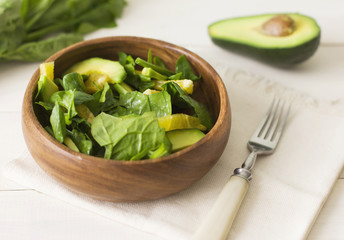 Raw salad of spinach, avocado and orange on a white wooden background