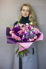 Beautiful blonde young woman holding in her hands delicate bouquet of flowers in rustic style