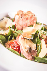Baby spinach, dry sausage, matured cheese, roast tomatoes, thyme-balsamic vinaigrette salad on a white background