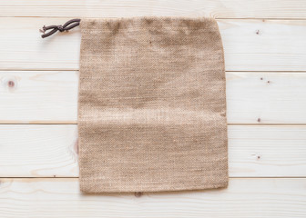 Jute hessian canvas tote bag with drawstring, mockup of small eco sack made from natural hemp burlap flat lay on white wood background from top view