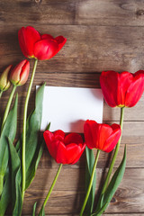 Row of red tulips on wooden background with space for message. Women's or Mother's Day background. Top view