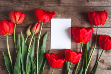 Fototapeta na wymiar Row of red tulips on wooden background with space for message. Women's or Mother's Day background. Top view