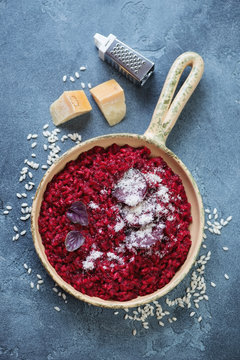 Frying pan with beetroot risotto and parmesan over blue stone background, above view, vertical shot