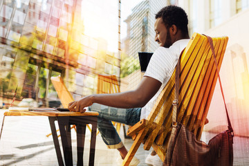 Lovely morning. Calm young handsome man having a good time while sitting alone in a nice comfortable cafe and feeling relaxed while looking at his modern device