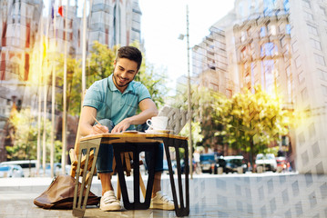 Getting inspiration. Smart experienced creative journalist getting inspiration while sitting outside in a cafe with a laptop by his side and writing a new amazing article for a popular magazine