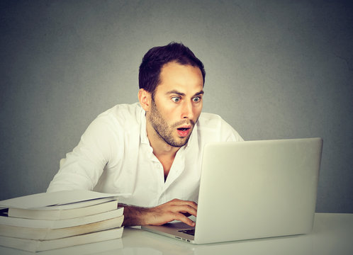 Shocked man watching laptop while studying