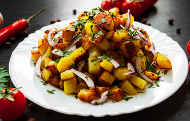 fried potatoes with bacon and onion in a plate on a dark wooden background
