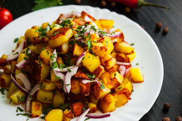 fried potatoes with bacon and onion in a plate on a dark wooden background
