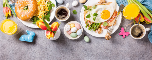 Easter breakfast flat lay with scrambled eggs bagels, orange tulips, bread toast with fried egg and green asparagus, colored quail eggs and spring holidays decorations. Top view. Copy space.