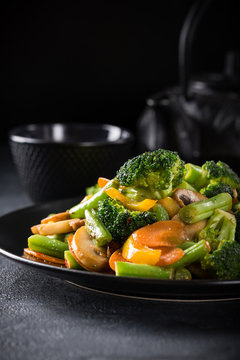 Hot stir fried vegetables on black plate. Healthy asian food concept with copy space.