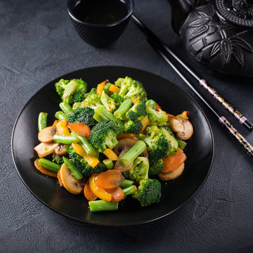 Hot stir fried vegetables on black plate. Healthy asian food concept.