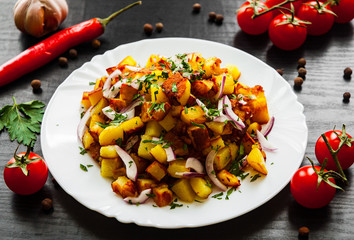 fried potatoes with bacon and onion in a plate on a dark wooden background