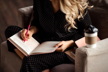 Cropped shot of unrecognizable blonde female writes down information in notebook or diary, prepares...