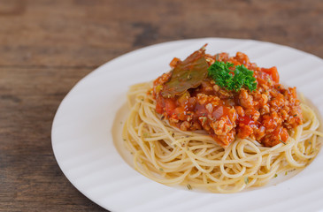 Spaghetti bolognese sauce with beef or pork,cheese,tomatoes and spices on white plate on wood table in close up view with copy space. Homemade delicious Italian traditional food for lunch or dinner.