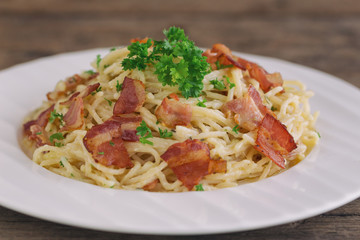Spaghetti carbonara with bacon and cheese on white plate sprinkle with chopped parsley on wood...