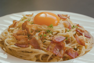 Spaghetti carbonara with bacon, cheese and egg yolk on white plate sprinkle with chopped parsley in close up view. Italian traditional homemade food for lunch or dinner so creamy and delicious.