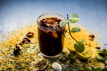Mixed fruit juice/shrabat with ingredients like lemon,lemon juice, mint leaves, orange juice, etc in a transparent glass on silver wooden surface.