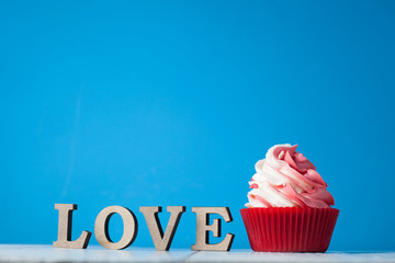 Cupcake with red and white cream in red paper form with wooden letters with the word love on a light background