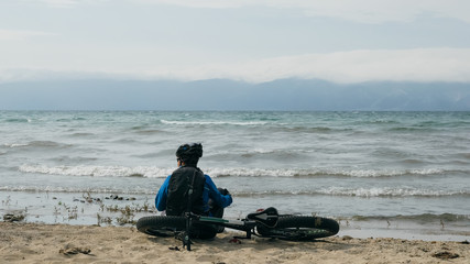 Fat bike also called fatbike or fat-tire bike in summer driving on the beach. The guy sits on the wheel of his bicycle, looks at the sea.