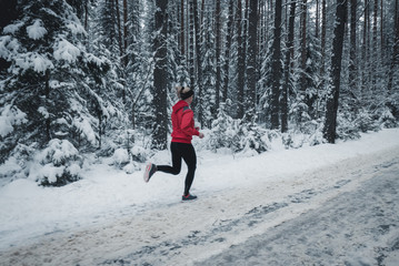 Athletic fit Caucasian female jogging in winter forest, trees covered with snow