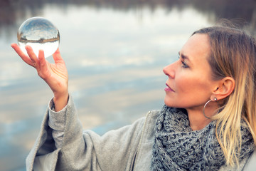 woman in front of lake holding up a glass ball