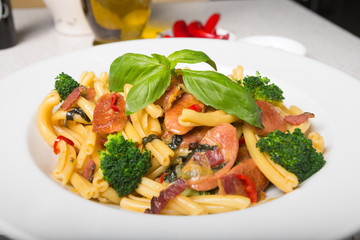 A delicious fresh gourmet Italian strozzapreti pasta dish, with pancetta, italian sausage, broccoli, vegetables, topped with fresh basil.