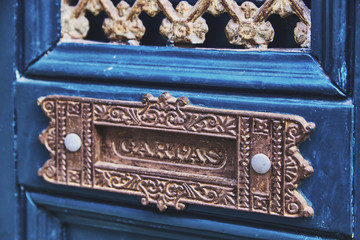A hole for mail in a blue wooden door, handmade by metal. Slot for correspondence is decorated with ornament. Close-up, macro.