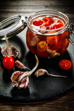 Tomatoes in jar on wooden background