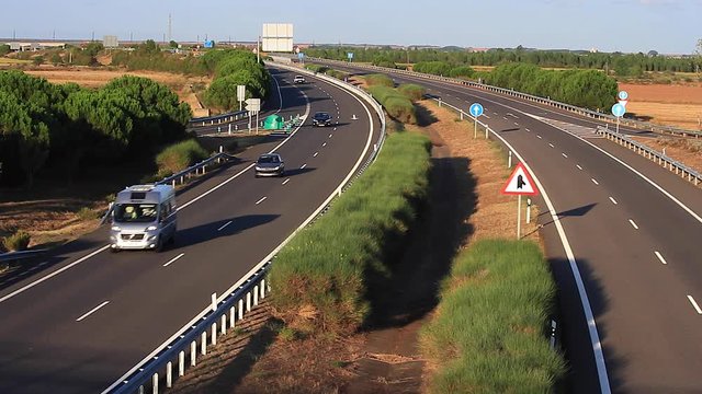 Vista general frontal  con luz de  atardecer  de trafico en los dos carriles de autopista o autov&iacute;a separados por setos, visto desde paso elevado