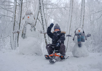 Fototapeta na wymiar boy on a sled and snowman in the woods