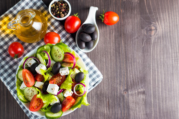 Fototapeta premium Fresh Greek salad made of cherry tomato, ruccola, arugula, feta, olives, cucumbers, onion and spices. Caesar salad in a white bowl on wooden background. Healthy organic diet food concept.