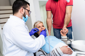 Obraz premium Attractive bearded man with his pregnant wife having medical treatment in dental office