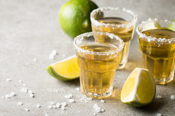 Macro focus photo of shots of golden Mexican tequila with lime and salt on wooden background. Alcoholic drink concept.