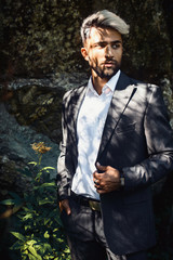 Fototapeta na wymiar Brutal young businessman with beard gray. Stylish Afghan man in jacket costume on the nordic Karelian nature landscape background. Marble Canyon and Dramatic sky in Karelia republic. Karelian fores