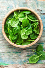 Fresh baby spinach leaves in bowl on wooden background