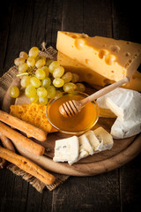 Slate board with various cheese and a glass of red rose wine. Brie. Camembert. Gouda, Masdaam, Roquefort, Cheddar and grapes on a wood with nuts, honey, crackers, blue cheese. Italian, French cheese.