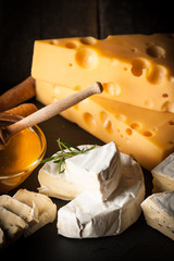 Slate board with various cheese and a glass of red rose wine. Brie. Camembert. Gouda, Masdaam, Roquefort, Cheddar and grapes on a wood with nuts, honey, crackers, blue cheese. Italian, French cheese.