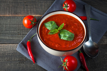 Chili tomato soup with sour cream sauce, cottage cheese, basil and red hot peppers on wooden background. Healthy, vegan and dieting lunch and dinner concept.