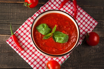 Chili tomato soup with sour cream sauce, cottage cheese, basil and red hot peppers on wooden background. Healthy, vegan and dieting lunch and dinner concept.