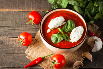 Chili tomato soup with sour cream sauce, cottage cheese, basil and red hot peppers on wooden background. Healthy, vegan and dieting lunch and dinner concept.