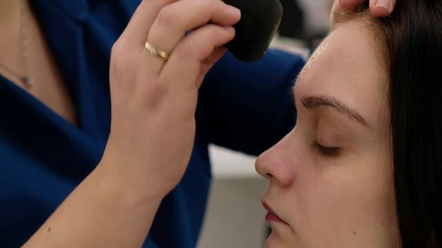 Make-up artist using sponge to apply pressed powder on face model