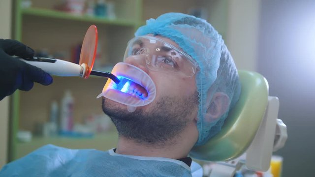 Doctor and patient with retractor in the dental office, cleaning with ultraviolet light and orange protective screen