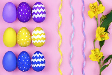 Happy Easter concept. Violet, yellow and blue easter eggs, colorful tapes and yellow flowers on pink background