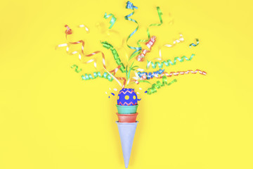 Happy Easter concept. Colorful waffle cone with colorful easter egg with curved tapes on yellow background