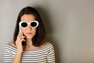Woman in a white striped top and white sunglasses talking on a smartphone.