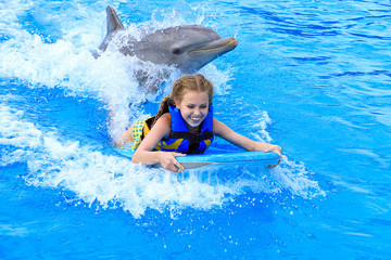 smiling Caucasian girl on wake board with dolphin in swimming pool