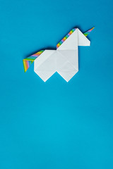Handmade white trendy geometrical polygonal paper origami unicorn on blue background. Empty space. Vertical poster, postcard, banner template. © mykolastock