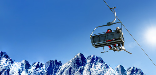 Composite image of skiers on a ski lift in high mountains on the background of a clear blue sky...